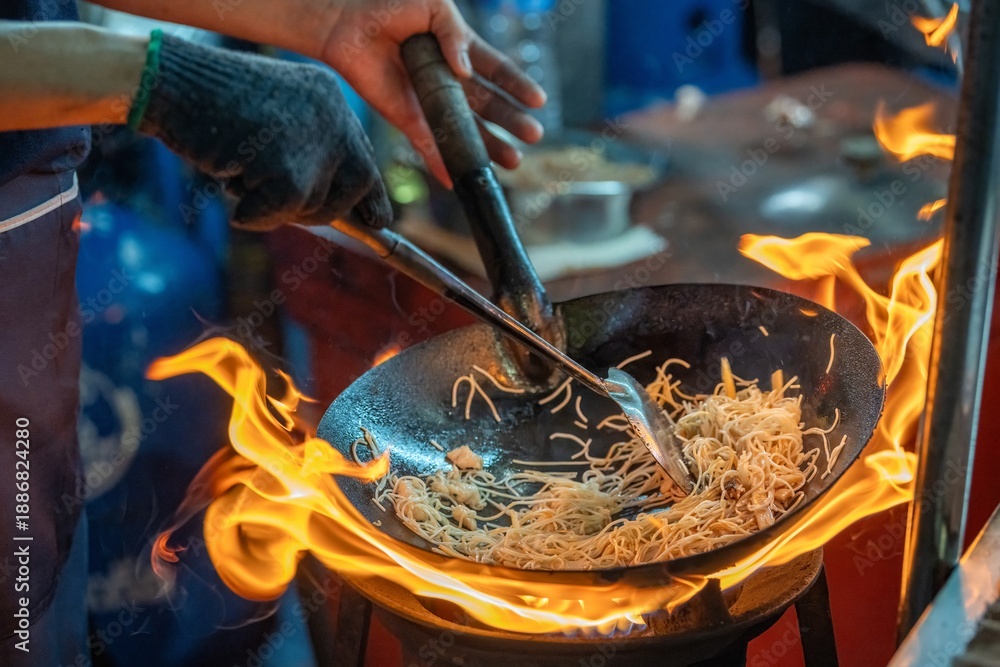 Obraz premium Pad Thai noodles is fried noodles cook in pan with big fire flame is hong kong style. Pad Thai famous Asian Thai street fast food in hot pan, Pad Thai is fried noodle dish a street food Thailand