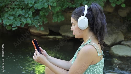 Pretty Hispanic woman listening to music with her headphones in a natural setting 