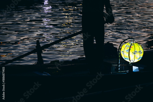 Foto Silhouette of person rowing boat with glowing lantern on water at night