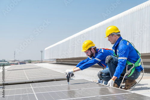 Two solar panel installation workers wearing safety gear are installing solar panels on a commercial building's roof.