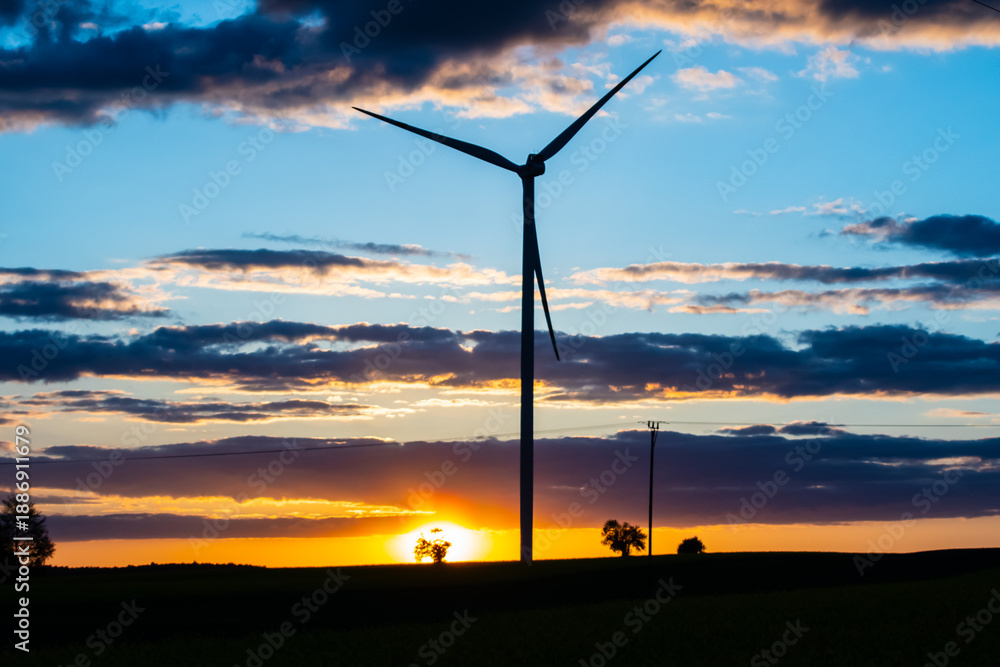 Obraz premium Single wind turbine silhouette against a blue and orange sunset sky