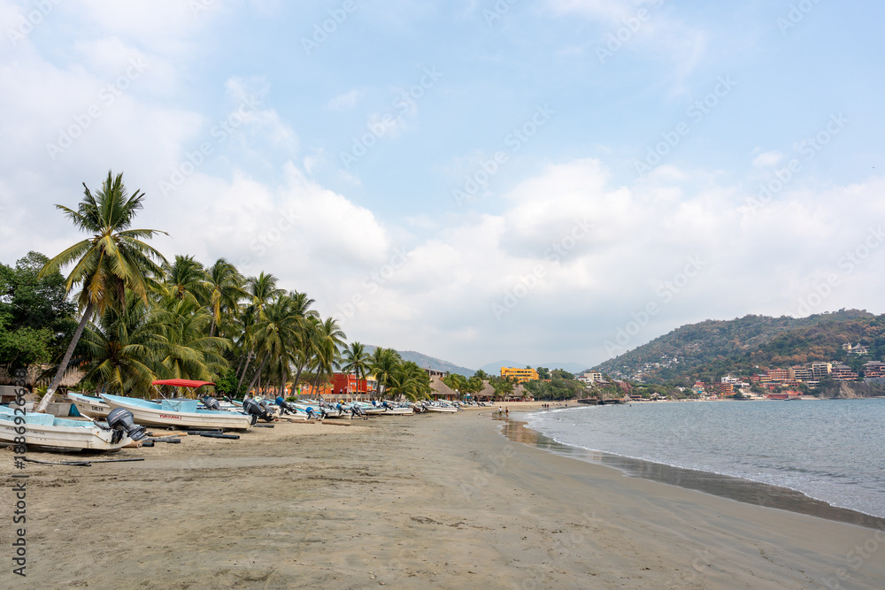 Fototapeta premium View of the beach in the bay of Ixtapa Zihuatanejo with boats in the sea and palm trees on the sand. Tropical landscape of costa grande, Guerrero. Mexico, January 19, 2026.