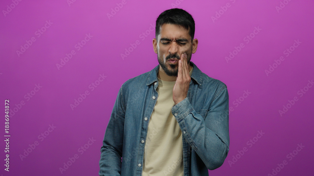 Fototapeta premium Man suffering toothache against pink background looking uncomfortable and distressed while touching his cheek.