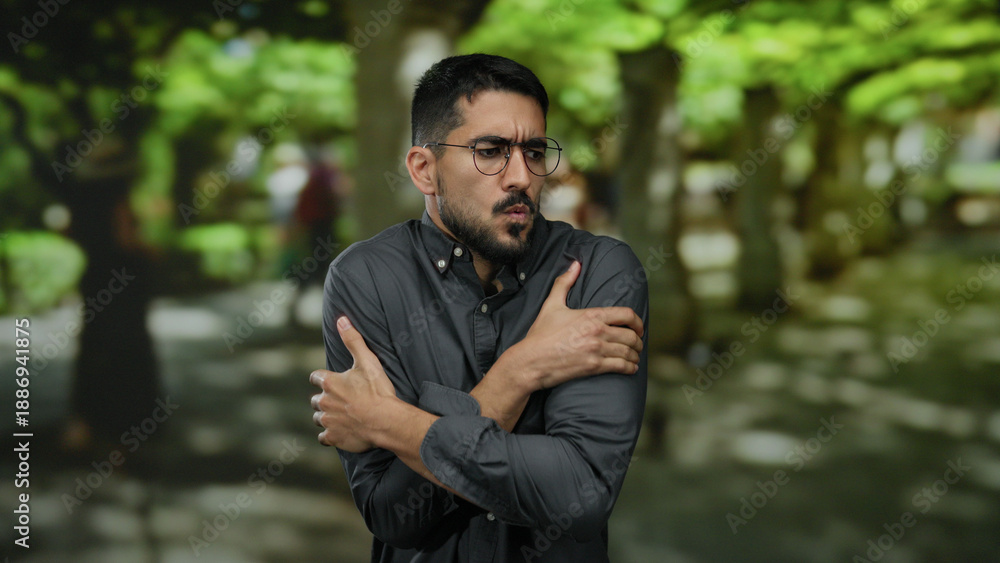 Fotografie Young man shivering in park outdoors on a chilly day showing cold discomfort sur