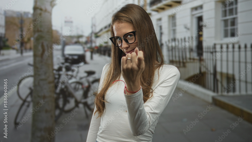 Fototapeta premium Woman in glasses beckoning with finger on a city street, hand extended toward camera; playful invitation.