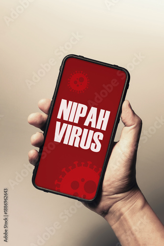 Hand holding smartphone with Nipah virus outbreak alert message on red screen background. Digital warning concept.