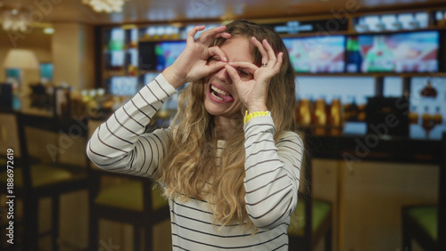 Cuadro en lienzo Woman holds her hands while smiling inside a cafe where a blonde young guest makes a playful binocular gesture looking very happy