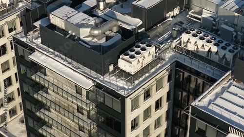 Drone footage shows a modern apartment building rooftop in winter, featuring snow-covered surfaces, ventilation ducts, HVAC units, and contemporary urban architecture.