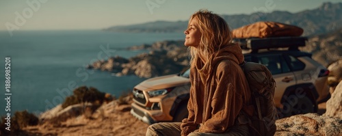 Woman traveler rests on a rocky coastal cliff with backpack beside an SUV on a scenic sea view road trip