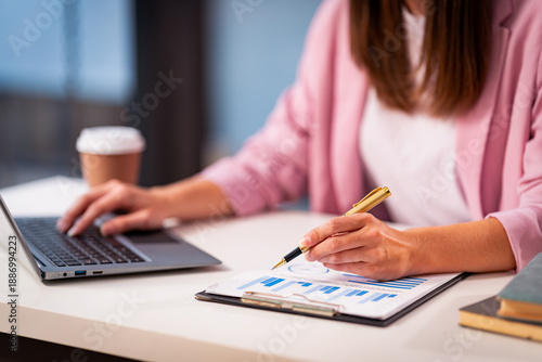 Fotografija A young woman is analyzing finances, typing on a laptop, demonstrating the use of computers to process data quickly and accurately