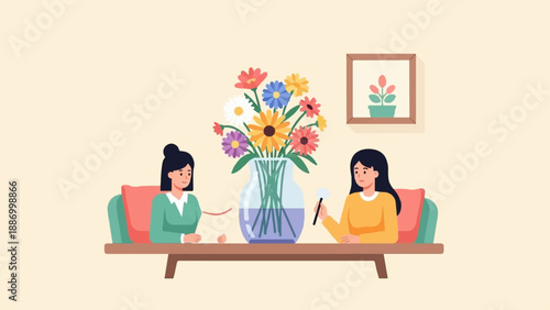 Two women sit across from each other at a table with a vase of flowers