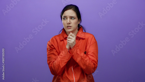 Bilde på lerret Woman with brunette hair wearing orange prison jumpsuit stands in front of purple background, appearing worried