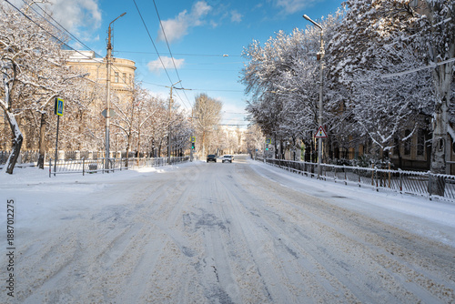 Winter city street. Roads and sidewalks are covered with snow. A sunny January day. After a heavy overnight snowfall. New Year's Morning. Old houses. Cars at traffic lights. The road is almost empty.