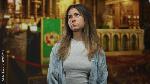 Canvas-taulu Woman looks up toward an ornate altar and green banner inside a catholic church building, standing near rope barrier; contemplation faith solace