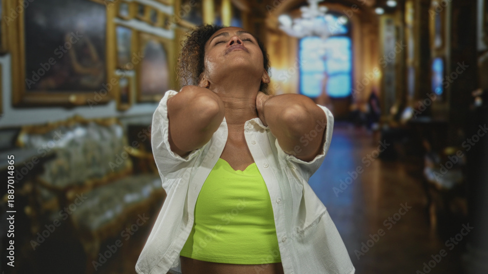 Obraz premium Woman wearing neon green top and open white shirt, hands on neck and face tilted back in museum gallery; pain.