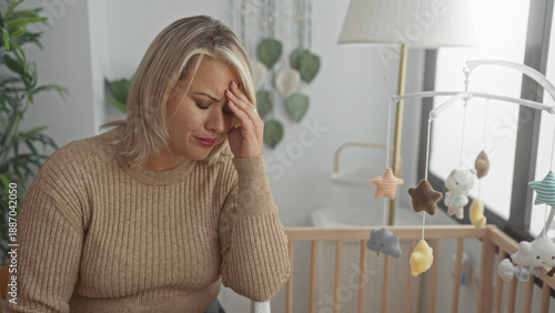 Quadro em tela Woman touching forehead beside wooden crib and hanging plush mobile in bright bedroom; maternal anxiety