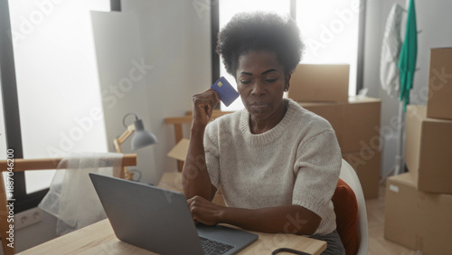 Photos Woman using laptop in new apartment surrounded by moving boxes holding credit ca