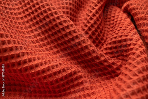 Abstract fabric background. Terracotta waffle fabric texture with folds and waves close-up. Natural cotton textiles for blanket, bath or kitchen towel, bathrobe, bedspread. Eco-friendly home material