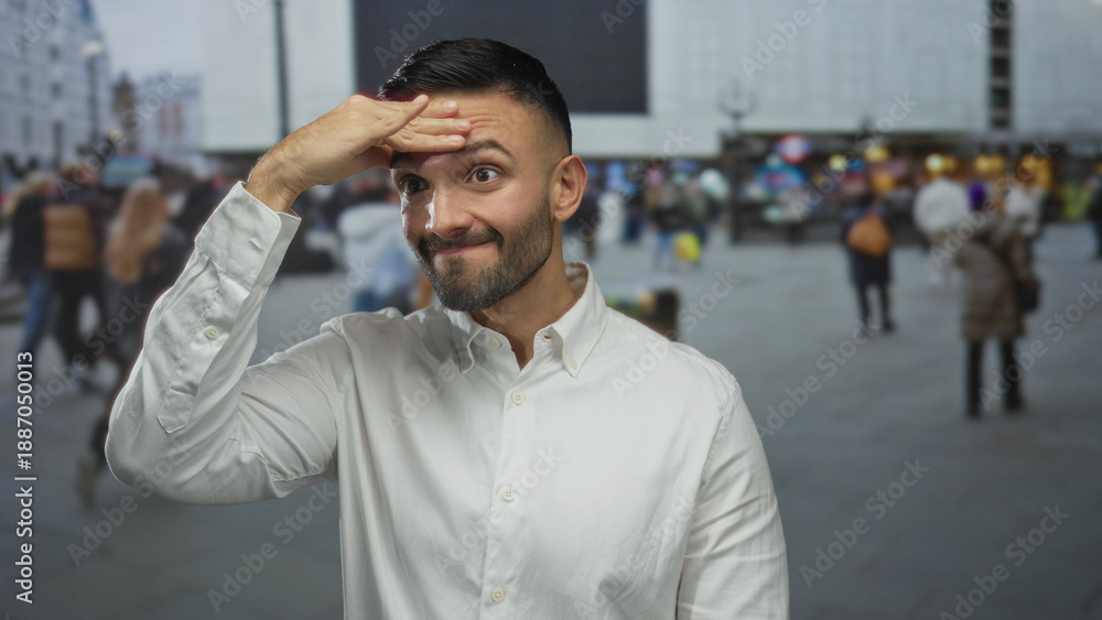 Obraz premium Young hispanic man on urban street outdoors looking thoughtful with hand on forehead as diverse city crowd blurs by in background.