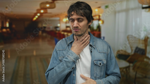 Quadro su tela Man in denim jacket clutches throat and presses stomach with other hand for sudden pain in building; unease urgency caution