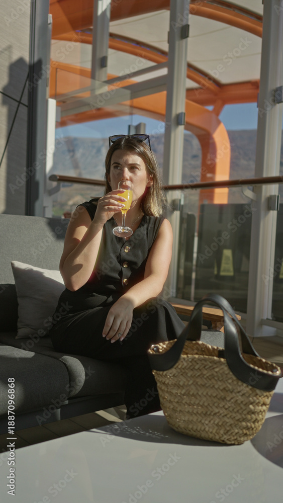 Fototapeta premium Woman holding a glass of orange juice on a cruise terrace with straw bag and sunglasses on head; relaxed vacation.