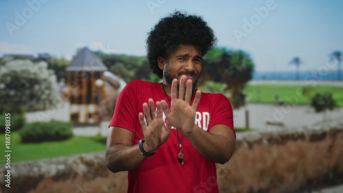 Fotografi Lifeguard man in red shirt with gesture of rejection in outdoor park setting wit