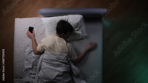Man sleeping in bed with a phone in his hand, struggling with restlessness and insomnia due to screen time before bed, highlighting technology addiction and poor sleep habits