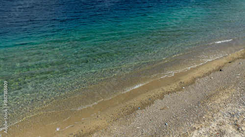 Canvas Print High-angle aerial view of a shoreline with clear, turquoise water transitioning to deep blue, meeting a sandy and pebbly beach