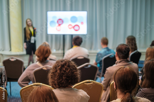 Wallpaper Mural Presenter delivers lecture to attentive audience in conference room. Audience sits in chairs focusing on screen with colorful slides. Bright lighting creates professional learning atmosphere. Torontodigital.ca