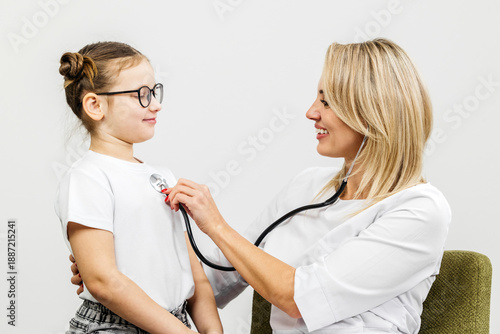 Bilde på lerret Female doctor using stethoscope to examine young girl in white shirt, both smili