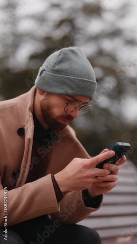 Young Man Sitting Outdoors, Engaged with His Smartphone on a Casual Day