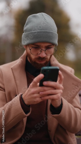 Young Man In Beanie And Glasses Using Smartphone Outdoors In Nature