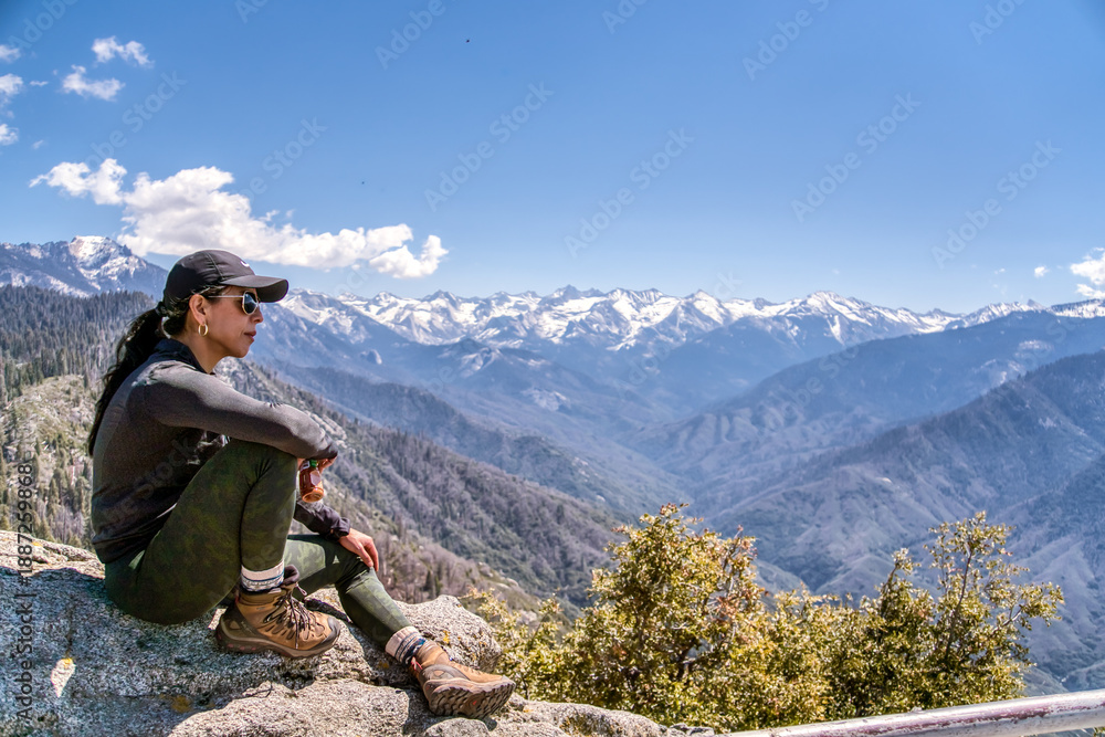 Fototapeta premium A woman is sitting on a rock overlooking a mountain range