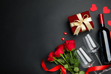 Beautiful velvet gift box, roses, wine with glasses and decorative hearts on black background, flat lay and space for text. Valentine's Day