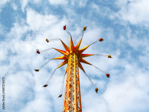 Картината върху платно Vibrant image of a tall chair swing amusement ride, captured from below against a partly cloudy blue sky