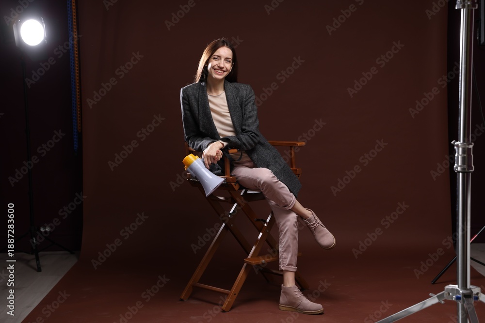Fototapeta premium Professional film director with megaphone on chair against brown background