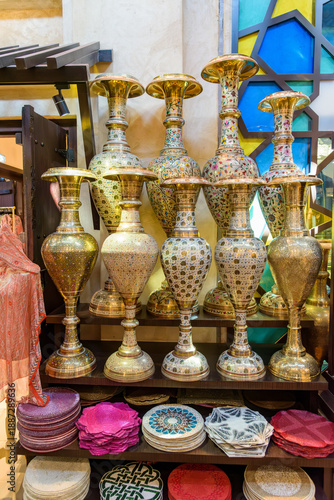 Traditional decorative brass vases and colorful handmade plates are displayed in an oriental shop