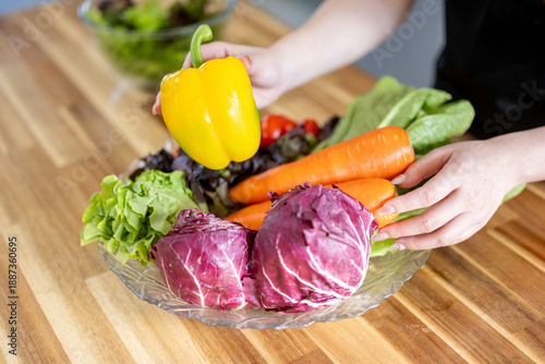 An Asian woman is arranging vegetables on a plate on a kitchen table, promoting the concept of healthy eating and dieting.
