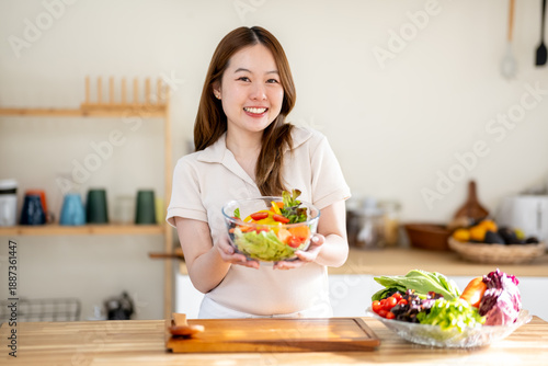 An Asian woman is making a salad in the kitchen. The concept is related to healthy eating and dieting.