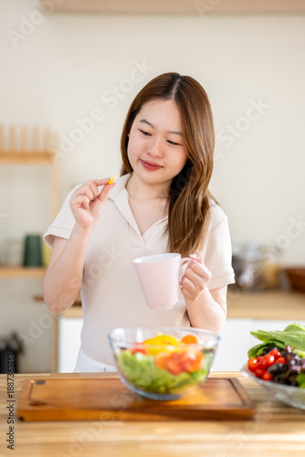 An Asian woman is taking vitamins in the kitchen. The concept of healthy eating and dieting.