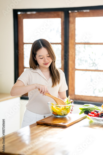 An Asian woman is making a salad in the kitchen. The concept is related to healthy eating and dieting.