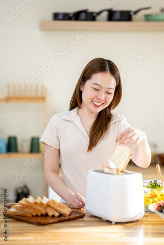 An Asian woman is happily toasting bread for breakfast in the kitchen.
