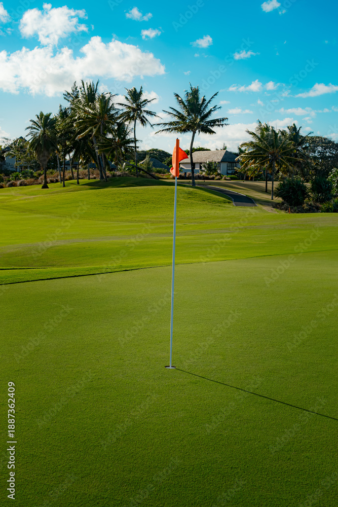 Obraz premium Golf green flag waving on tropical course under sunny sky.