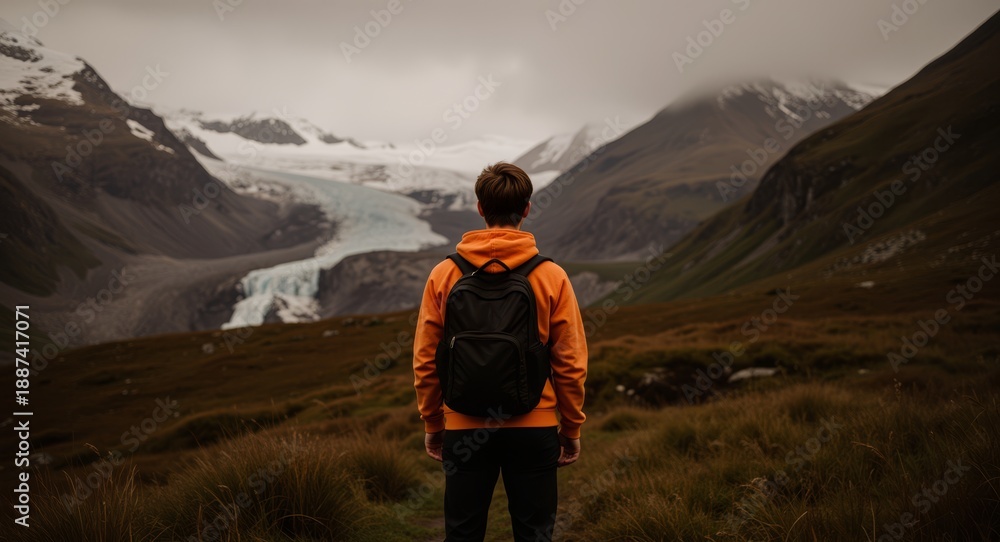 Fototapeta premium Einsamer Wanderer mit Rucksack blickt in weites Gletschertal mit schroffen Bergen, Graslandschaft und Wolkenhimmel – Symbol für Freiheit, Abenteuer, Naturverbundenheit und nachhaltiges Reisen