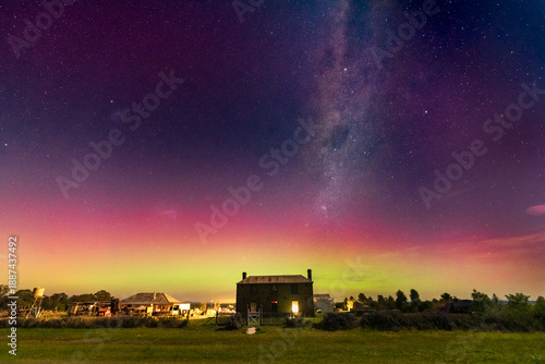 Low angled view of colourful Aurora Australis over an historic roadside farmhouse