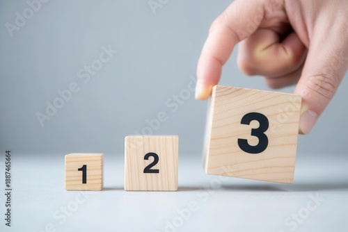 Hand placing wooden block number 3 next to blocks 1 and 2, concept of steps, sequence, or ranking