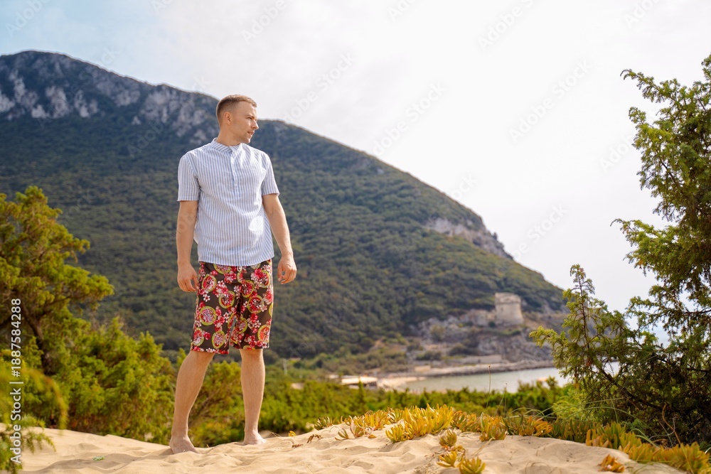 Naklejka premium Smiling Man on Sandy Dune with Green Hills and Sea