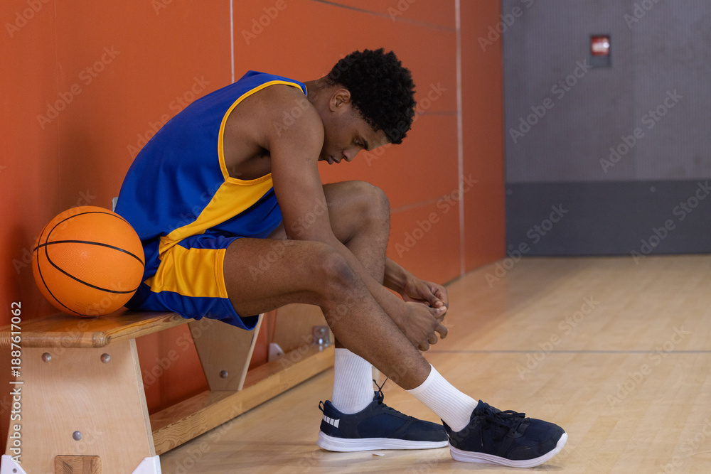 Obraz premium Basketball resting on wooden bench while sneakers are being tied on gym court lines
