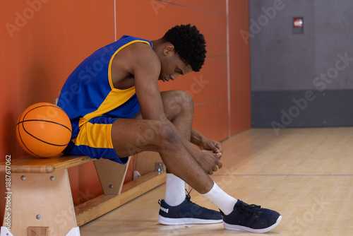 Basketball resting on wooden bench while sneakers are being tied on gym court lines