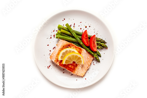 Garnished fried salmon steak with boiled green asparagus on white background. Top view